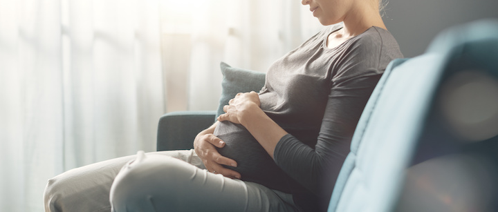 Pregnant woman sits on sofa